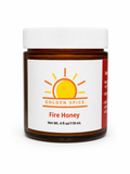 An amber glass jar of Golden Spice Fire Honey with a white screw cap and a white label featuring a yellow sun logo.